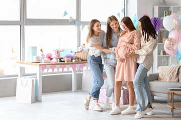 Female friends touching belly of young pregnant woman at baby shower party - obrazy, fototapety, plakaty
