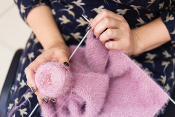 Hands of a woman knitting with pink wool, one hand holds a ball of thread for knitting	