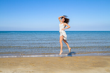 Carefree happy young woman feeling blissful jumping of joy on peaceful beach in summer morning. Stress free, relaxation, freedom wellness, happiness concept.
