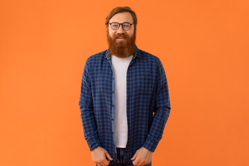 Smiling redhaired man with beard wearing glasses on orange background