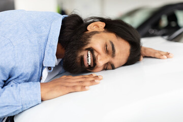 Man lovingly embracing a new car in showroom