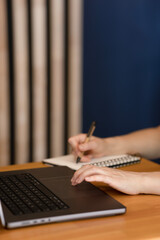 Female hand on open laptop running finger across touchpad, space for copy. Girl working in office writing with pen in notebook, laptop on wooden table, space for copy, text and advertising