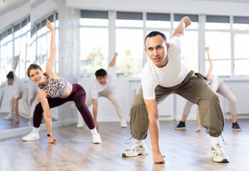 Group of young people, girls and guys in sportive casual style clothes dancing in choreography class