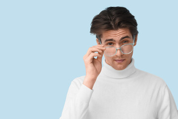 Young man in eyeglasses on blue background, closeup. Glaucoma awareness month