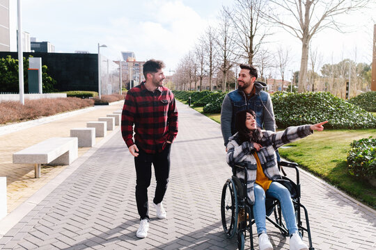 A woman in a wheelchair points something out to her friends during a pleasant walk in a city park.