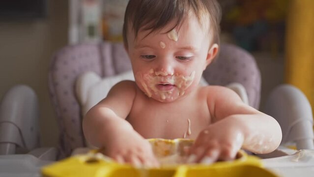 baby eats dirty. happy family a kid toddler concept lifestyle. baby girl dirty sitting messing with food at the table for feeding in the kitchen. grimy toddler in the kitchen