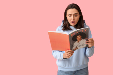 Fototapeta premium Shocked young woman reading beauty magazine on pink background