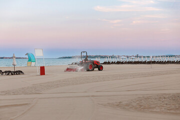 Tractor smoothes the sand on public beach by the sea