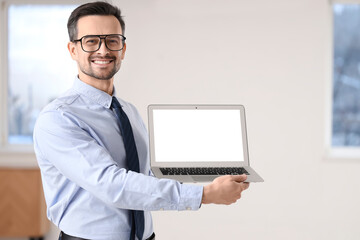 Portrait of male real estate agent holding laptop with blank screen in new apartment