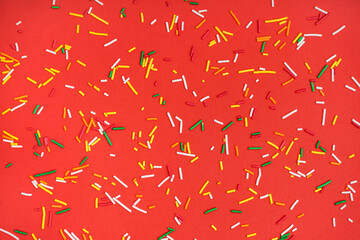 Sweet colorful sprinkles scattered on red background