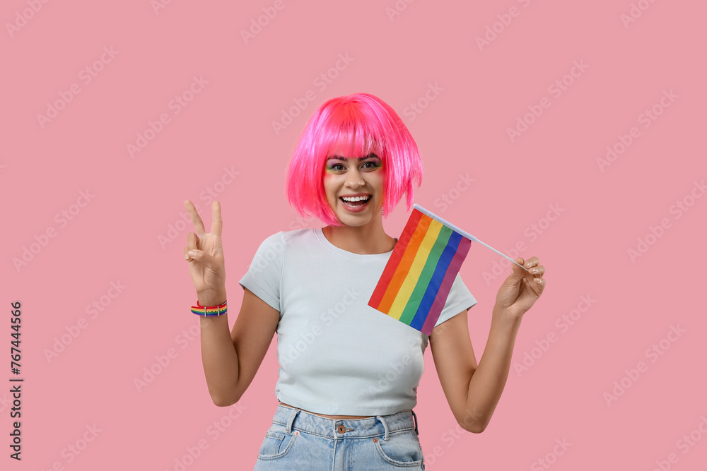 Poster Happy African-American woman with rainbow flag showing victory gesture on pink background. LGBT concept