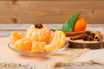 Plate with fresh tangerine segments and spices on wooden background