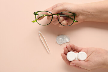 Female hand with eyeglasses, container for contact lenses and tweezers on beige background