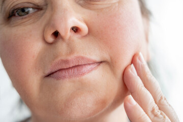 mature woman gently touches face, accepting visible signs aging such wrinkles, sagging skin and...