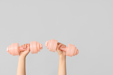 Female hands with dumbbells on grey background, closeup