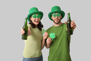 Beautiful young couple in leprechaun hats with bottles of beer and clover on grey background. St....