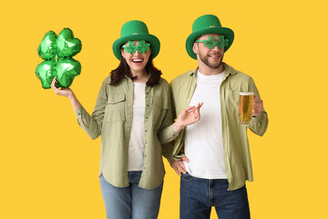 Beautiful young couple in leprechaun hats with glass of beer and air balloon in shape of clover on...