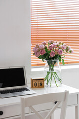 Calendar with date of International Women's Day, roses and laptop on table in office