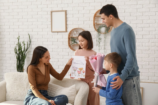 Family greeting their mother with Mothers Day with bouquet of tulips and drawing in living room