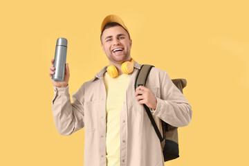 Male tourist with backpack and thermos on yellow background