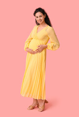 Happy young pregnant African-American woman on pink background