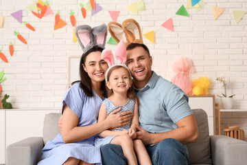Happy family in Easter bunny ears sitting on sofa at home - obrazy, fototapety, plakaty