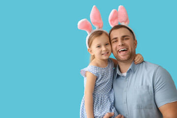 Happy young man with little daughter in Easter bunny ears on blue background