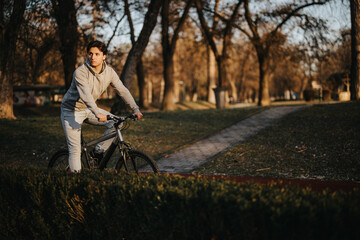 A contemplative young man with his bike takes in the tranquil atmosphere of a park at dusk, embodying a sense of leisure and fitness.