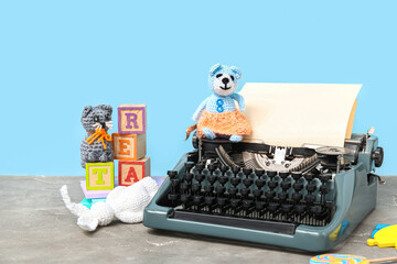 Beautiful composition with vintage typewriter and knitted toys on table near blue wall