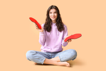 Young woman holding orthopedic insoles on beige background