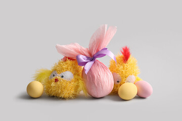 Painted and chocolate Easter eggs wrapped in paper with chick toys on grey background