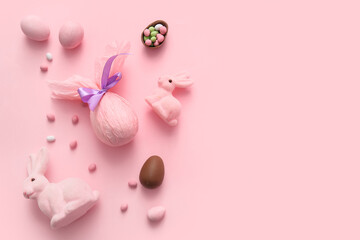 Painted and chocolate Easter eggs wrapped in paper with toy bunnies on pink background