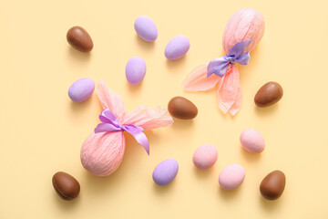 Painted and chocolate Easter eggs wrapped in paper on beige background