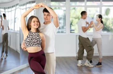 Photo sur Plexiglas École de danse Happy smiling modern young guy and girl enjoying impassioned merengue in latin dance class. Social dancing concept..
