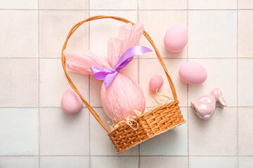 Wicker basket with painted and chocolate Easter eggs wrapped in paper on white tile background