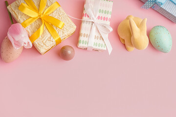 Painted Easter eggs with gift boxes, toy bunny and tulip flower on pink background