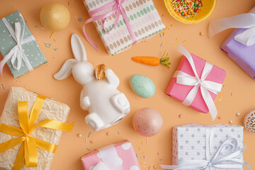 Painted Easter eggs with gift boxes and bunny on orange background