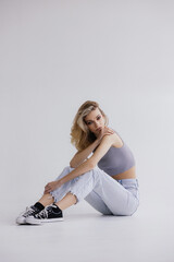 Fototapeta premium Full-length portrait of an attractive young girl in casual clothes, jeans, sneakers and a gray top.