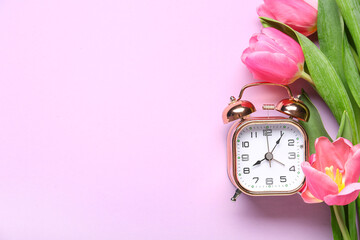 Alarm clock with tulip flowers on purple background