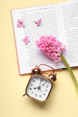 Alarm clock with book and hyacinth flowers on beige background