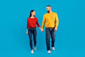 Man and woman are walking hand in hand against blue studio background