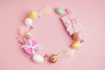 Beautiful wreath made of Easter eggs, feathers and gift boxes on pink background