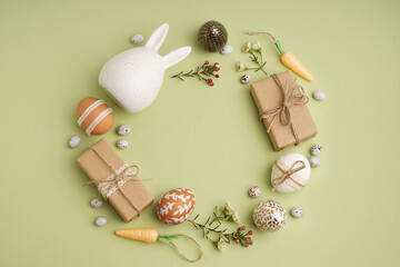 Beautiful wreath made of Easter eggs, flowers and gift boxes on green background © Pixel-Shot