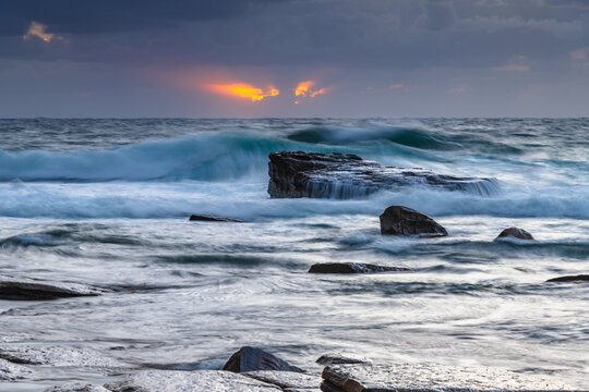 Moody sunrise seascape with clouds and casscades over the rock platorm at the rocky inlet