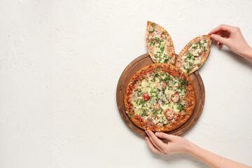 Female hands decorating pizza with Easter bunny ears on white background