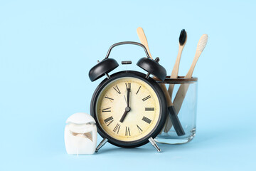 Black alarm clock, dental floss and toothbrushes on blue background