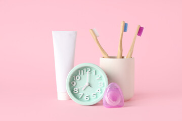 Clock, toothpaste, dental floss and toothbrushes on pink background