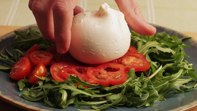 Burrata or Mozzarella cheese on fresh tomatoes and green arugula on plate close-up. From Italian cow's milk cheese made from mozzarella and cream.The outer casing is solid