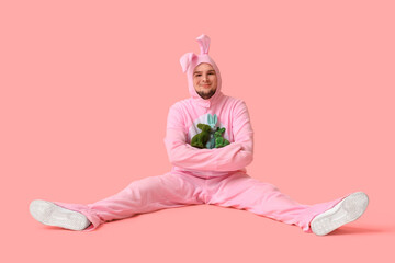 Young man in bunny costume with toy rabbits sitting on pink background. Easter celebration