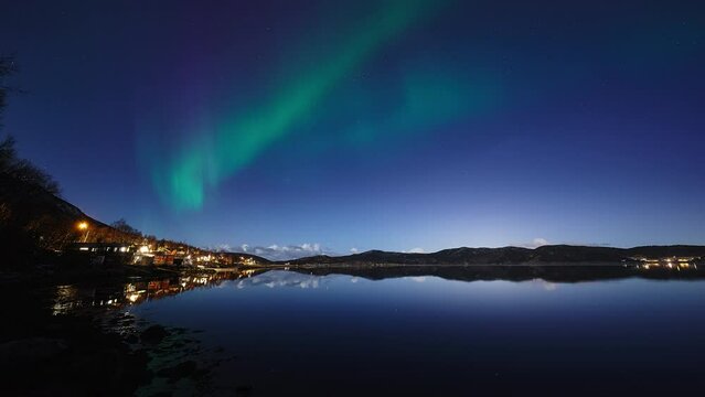A feint aurora dancing and mirroring itself in a crystal clear fjord, above a moonlit landscape in Bod&oslash; in March 2024.